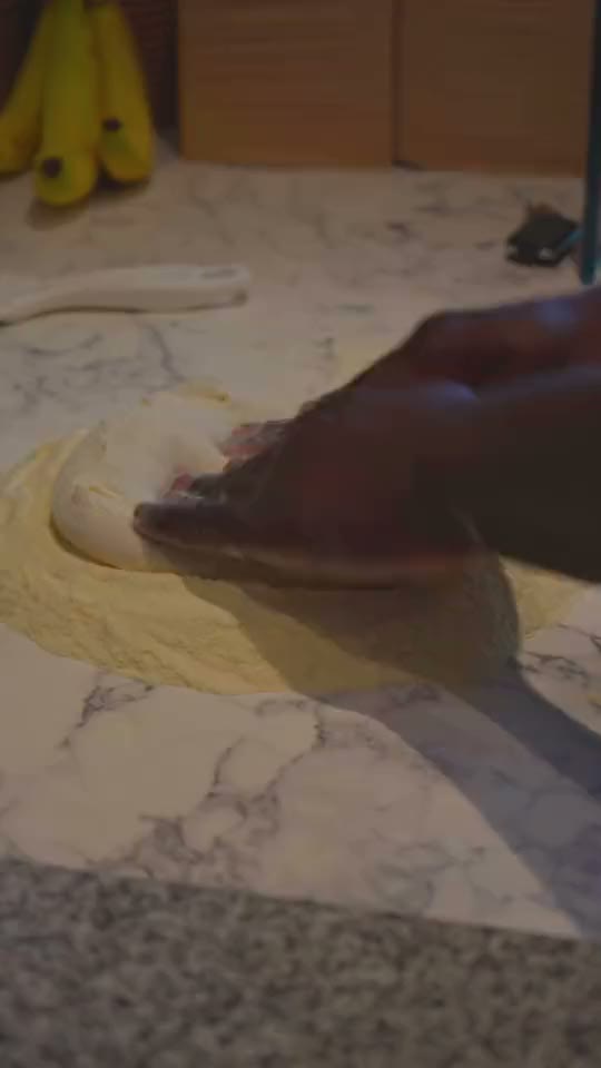Pizza dough being stretched by hand on a marble counter